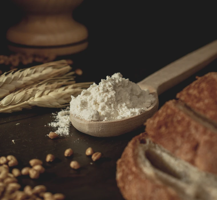 Ein Holzlöffel mit einem Haufen Mehl zwischen Getreide, Körnern und einem Brot